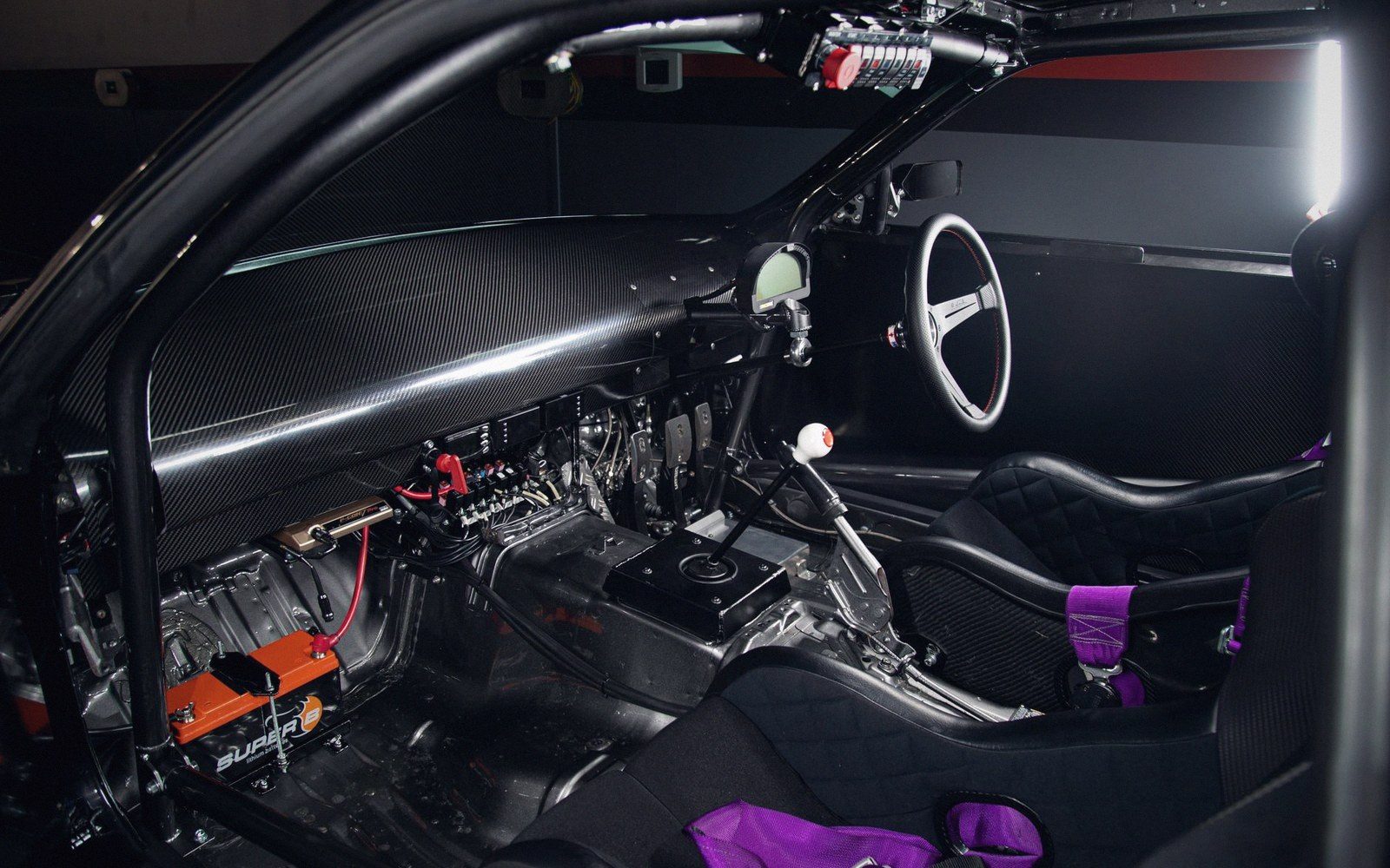 Stripped-down race car interior with roll cage, bucket seats and exposed wiring