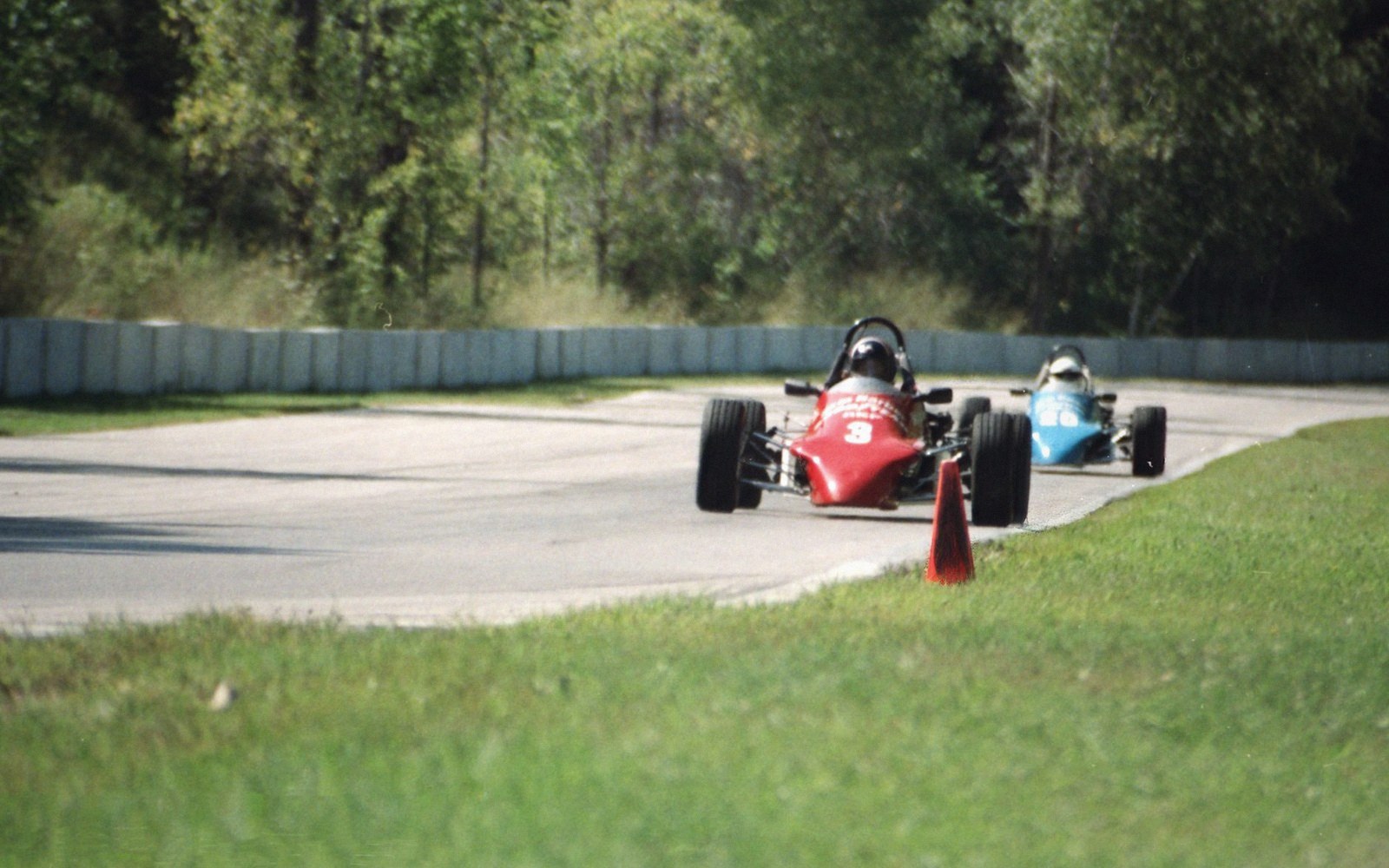 Red and blue open-wheel race cars round a curve on a paved track