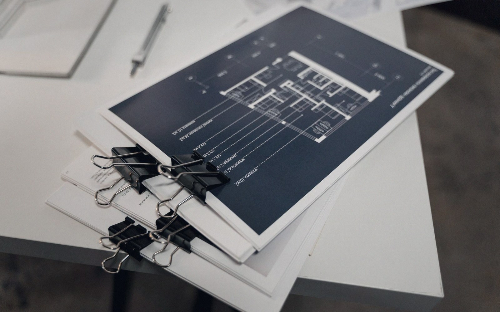 Architectural floor plan document bound with black binder clips on a desk