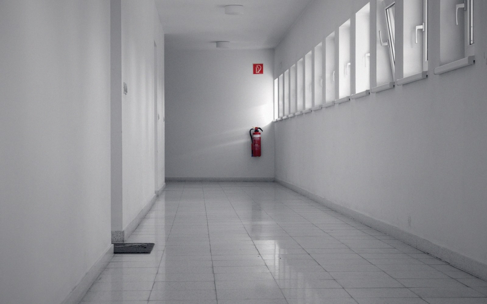 Empty white corridor with a red fire extinguisher mounted beside a row of tilted windows