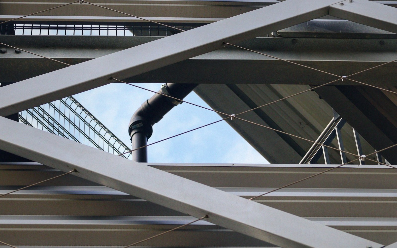 Crisscrossing steel beams and cables frame a black pipe against the sky