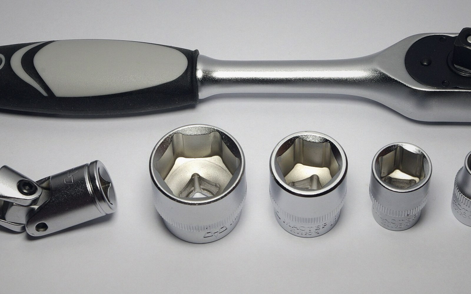 A ratchet handle beside a universal joint and several sockets of different sizes