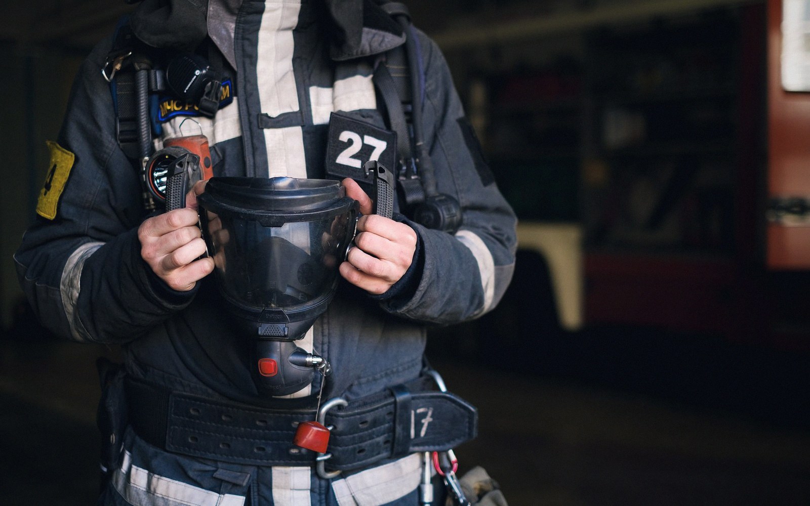 Firefighter in reflective gear holds a respirator mask against their chest