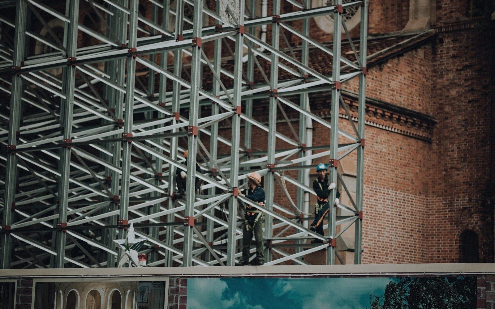 Workers in helmets stand on scaffolding against a brick building facade