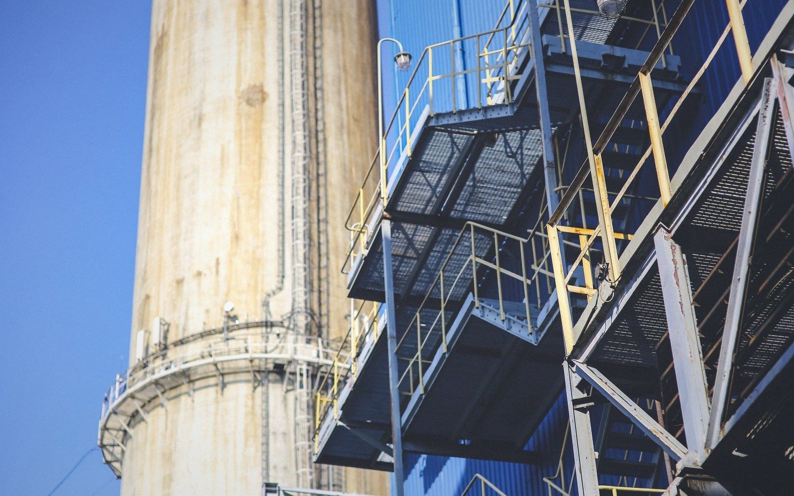 A galvanised scaffold tower against open sky on a backlot, blue matting stacked in its shade